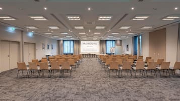Un salón de conferencias con filas de sillas, una pantalla de proyección y suelo alfombrado.