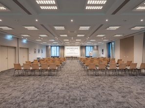 A conference room with rows of chairs, a projection screen, and a carpeted floor. - Mercure Parkhotel Mönchengladbach (Moenchengladbach)