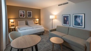 A hotel room with a bed, two bedside tables, a sofa, a small round table, and two wall-mounted lamps. - Mercure Parkhotel Mönchengladbach (Moenchengladbach)