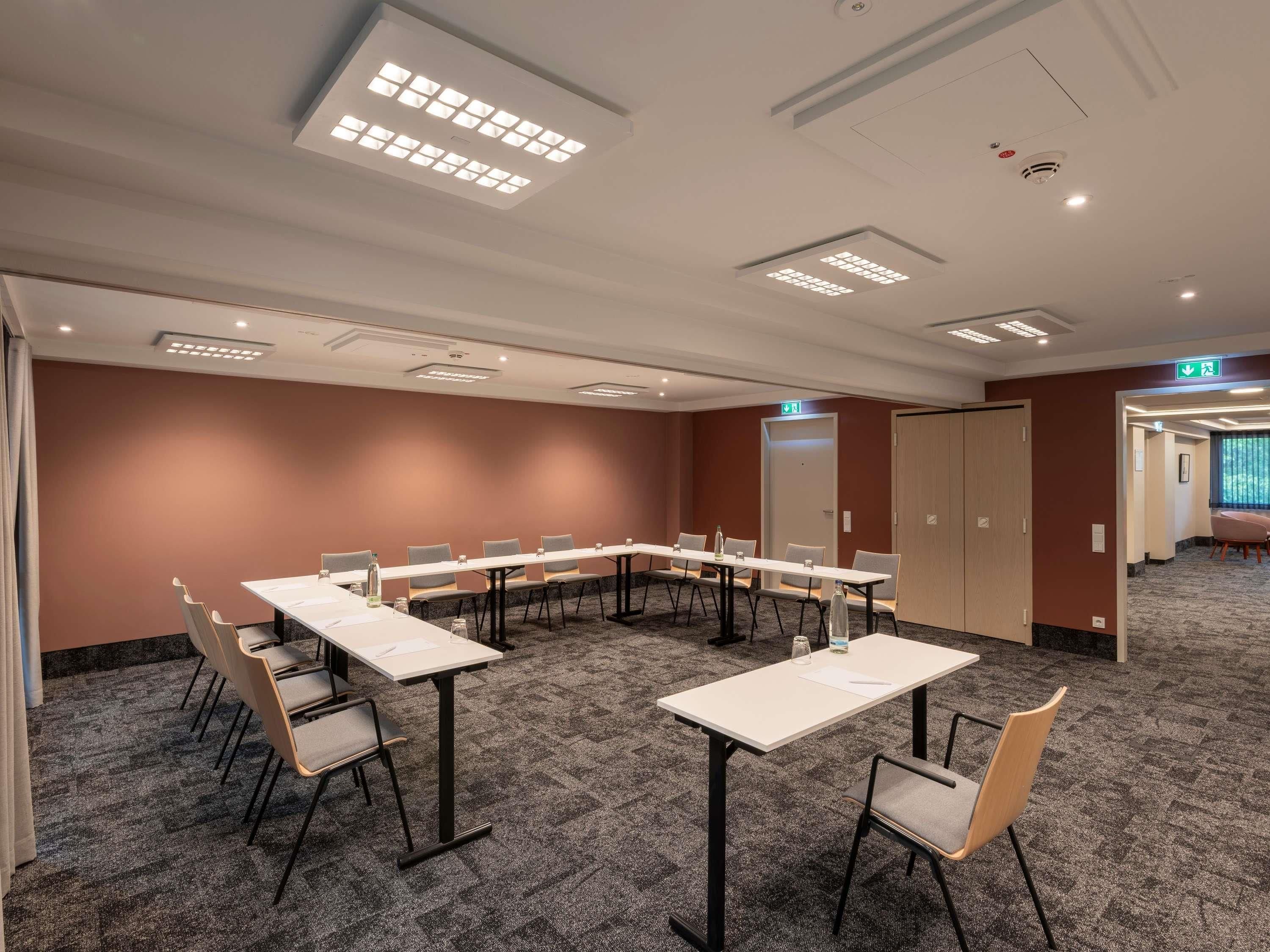 A conference room with a long table, chairs, carpeted floor, and ceiling lights.