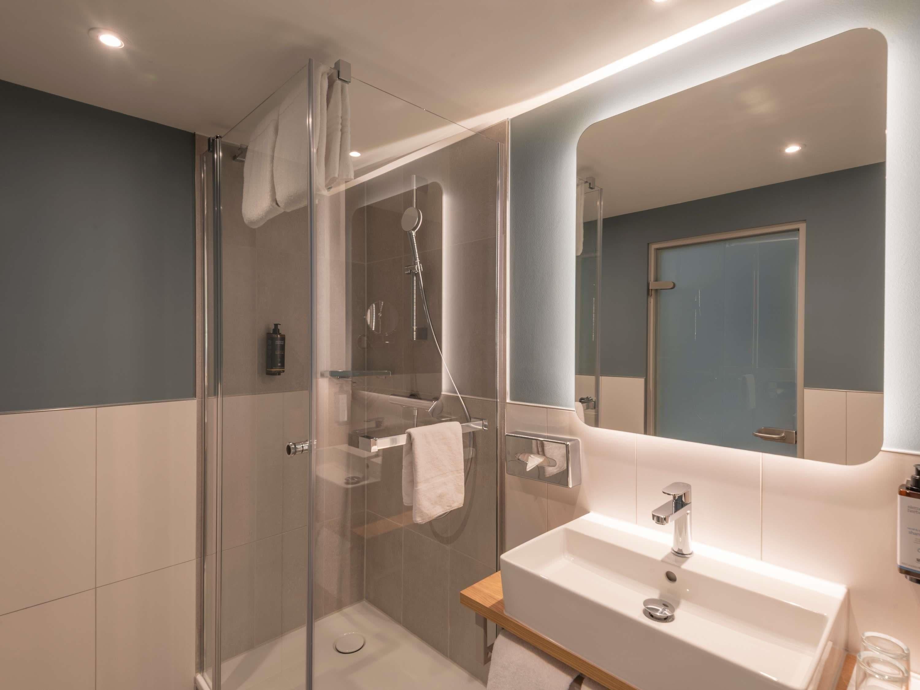Un baño moderno con cabina de ducha de vidrio, lavamanos blanco y un espejo grande.