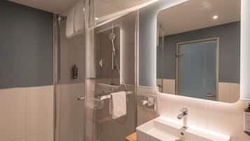 Un baño moderno con cabina de ducha de vidrio, lavamanos blanco y un espejo grande.