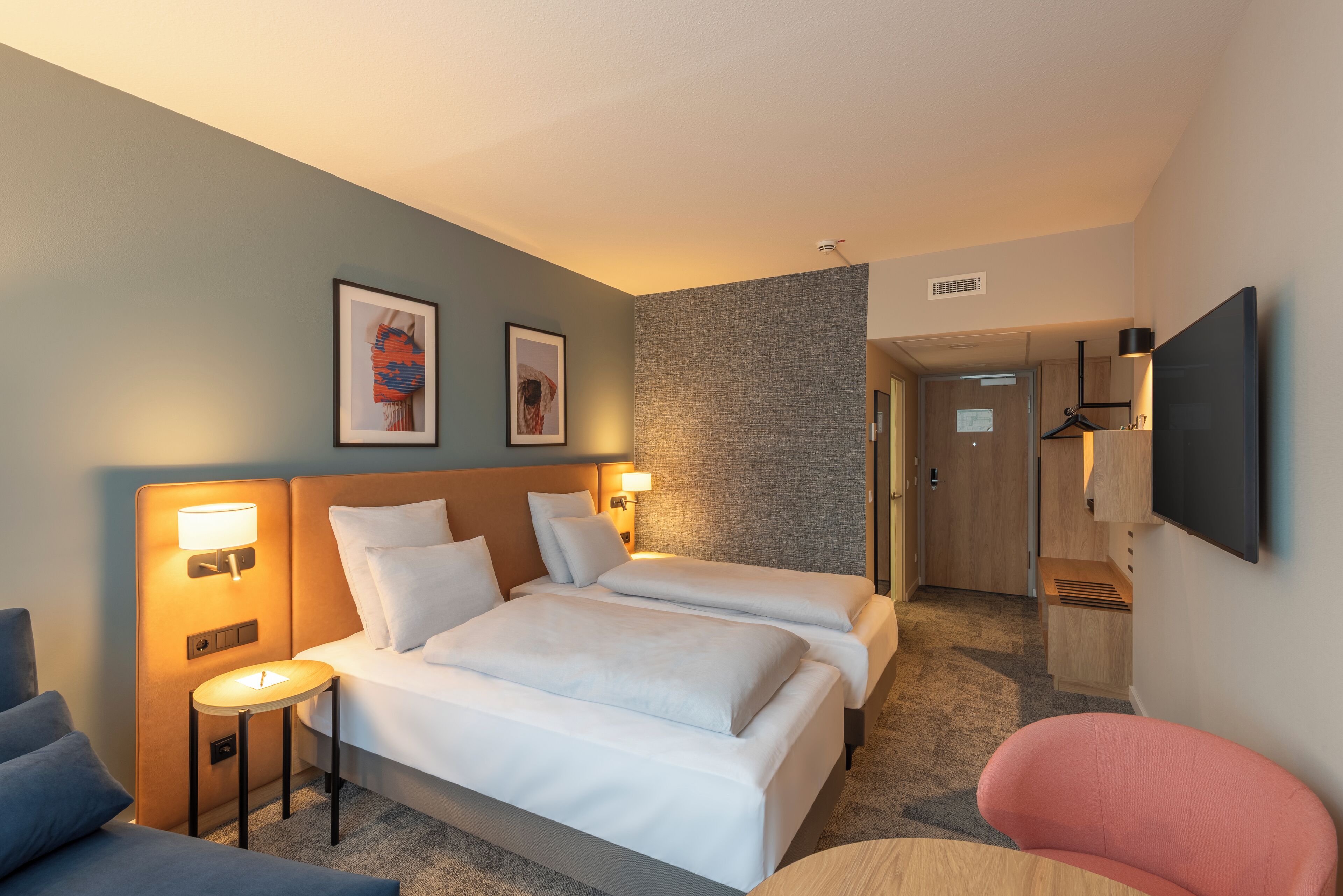 Habitación de hotel con dos camas, un escritorio, una silla y un televisor.