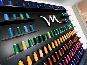 A wall with multiple shelves displaying spools of thread in various colors.