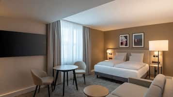 Habitación de hotel con una cama, dos sillones, una mesita, un sofá, un televisor y dos lámparas de pared.