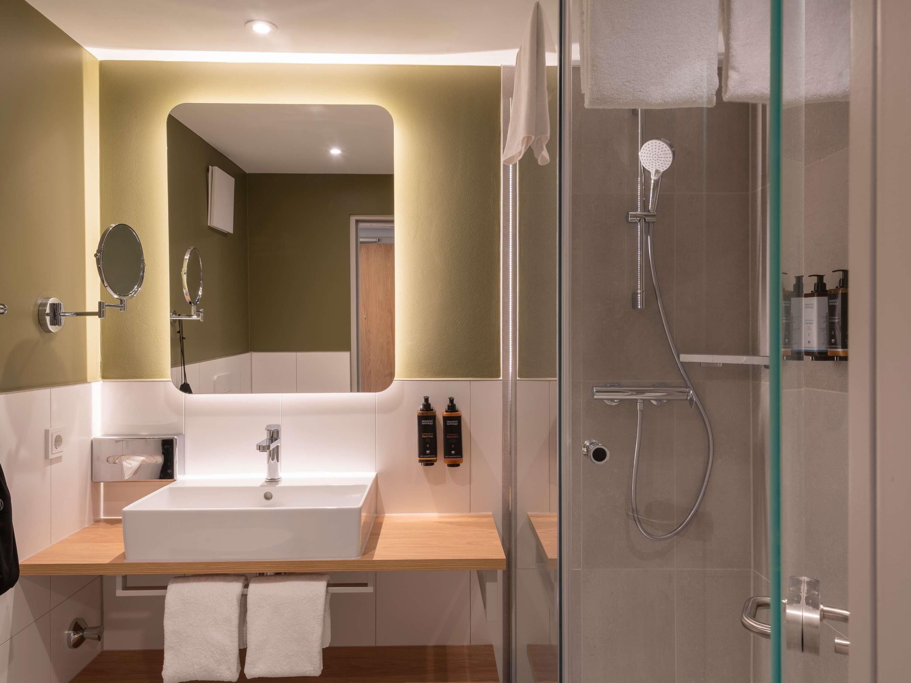 A modern bathroom with a large mirror, a sink, and a glass-enclosed shower.