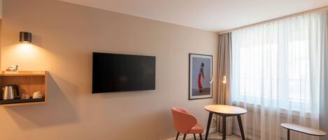 A hotel room with a flat-screen TV, a small table, a chair, a sofa, and a picture on the wall.