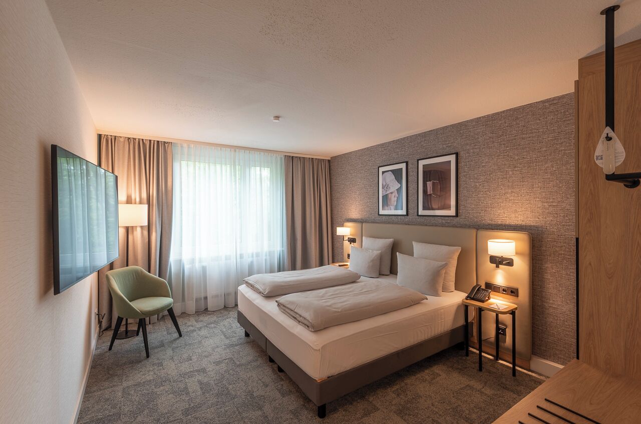A hotel room with a bed, a chair, a desk, and a television.