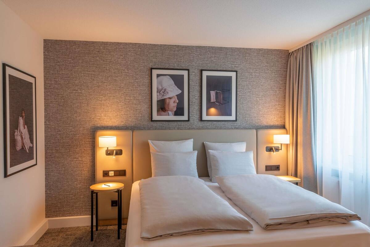 A hotel room with a large bed, two bedside tables, wall-mounted lamps, and framed pictures on the wall.