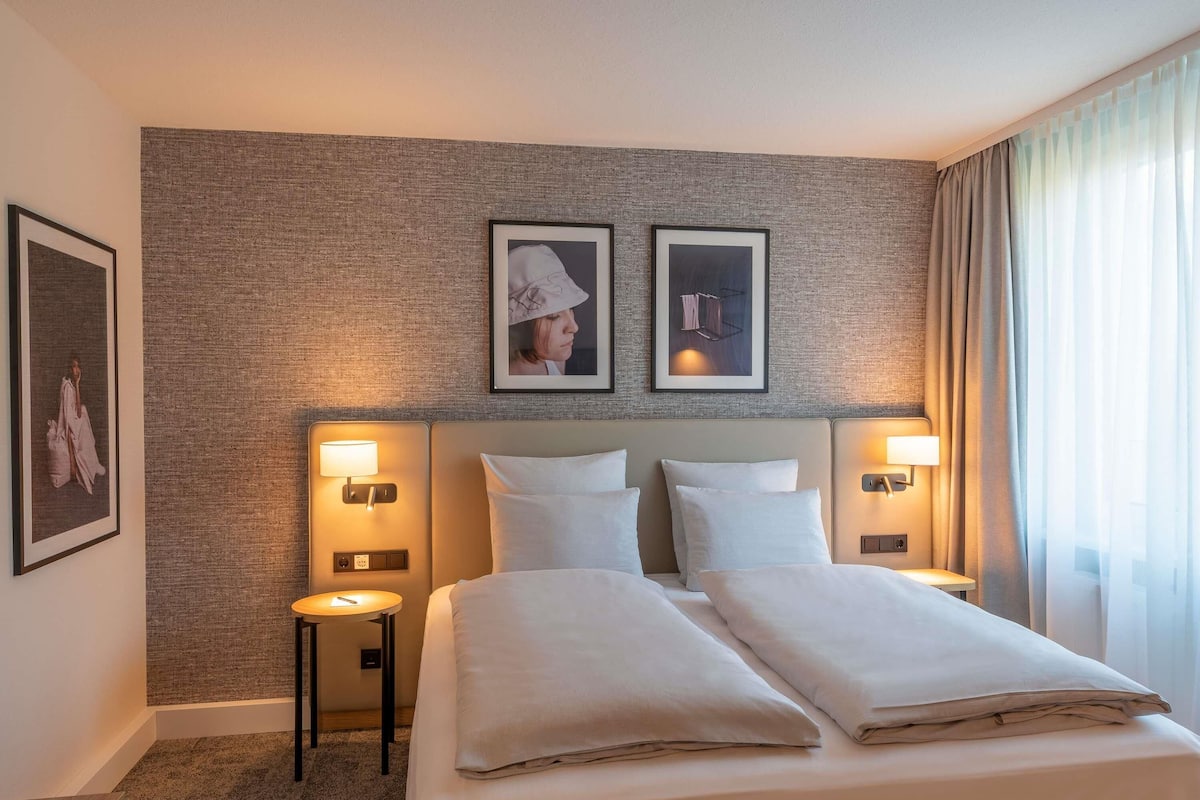 Ein Hotelzimmer mit einem großen Bett, zwei Nachttischen, Wandleuchten und gerahmten Bildern an der Wand.