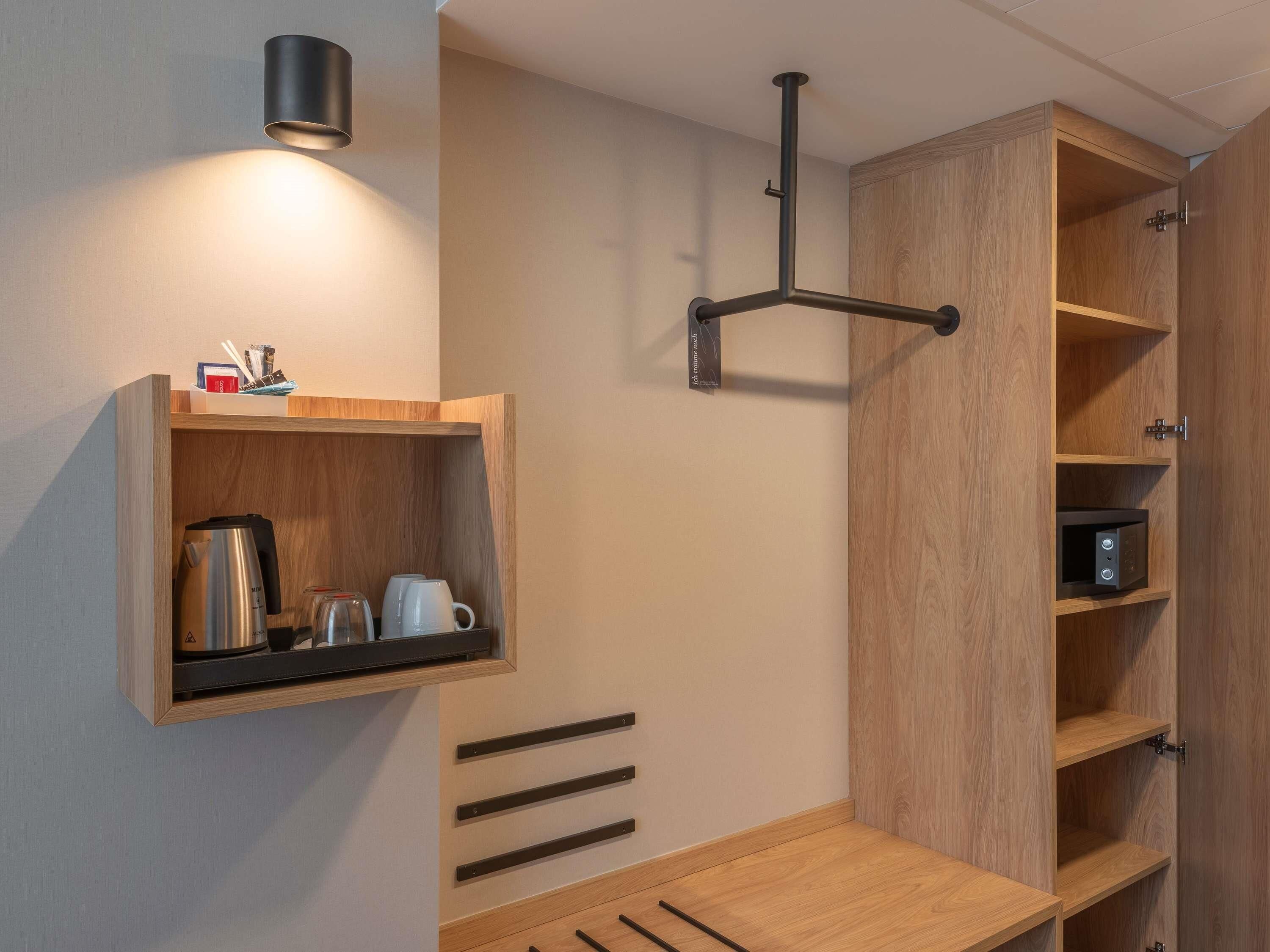 Une cuisine moderne avec des meubles en bois, un four à micro-ondes encastré et une bouilloire posée sur le plan de travail.