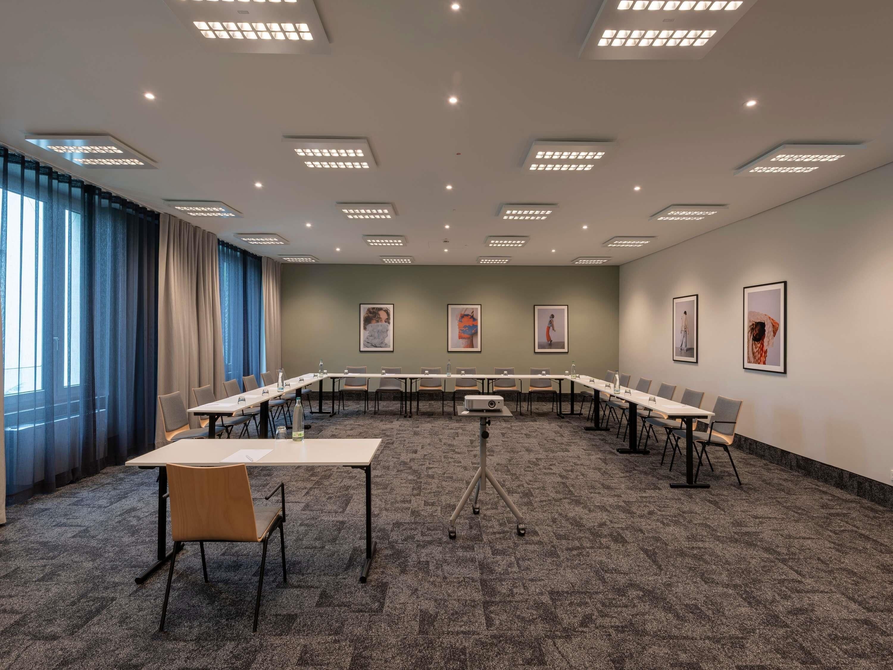 Ein Konferenzraum mit langem Tisch, Stühlen, einem Projektor und gerahmten Kunstwerken an den Wänden.