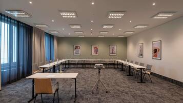 Ein Konferenzraum mit langem Tisch, Stühlen, einem Projektor und gerahmten Kunstwerken an den Wänden.