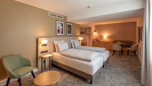 A hotel room with two beds, a desk, a chair, a round table, and a small kitchenette. - Mercure Parkhotel Mönchengladbach (Moenchengladbach)