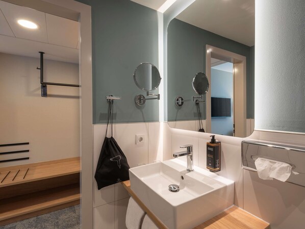 Un baño moderno con un lavamanos blanco, un espejo, un perchero para toallas y un secador de mano.