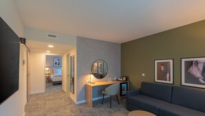 A modern living room with a grey sofa, a small round table, a desk with a chair, a mirror, and framed pictures on the wall. - Mercure Parkhotel Mönchengladbach (Moenchengladbach)