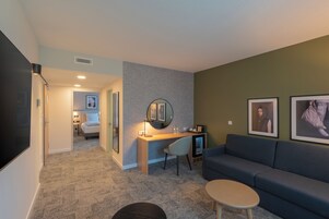 Una sala de estar moderna con un sofá gris, una pequeña mesa redonda, un escritorio con una silla, un espejo y cuadros enmarcados en la pared.