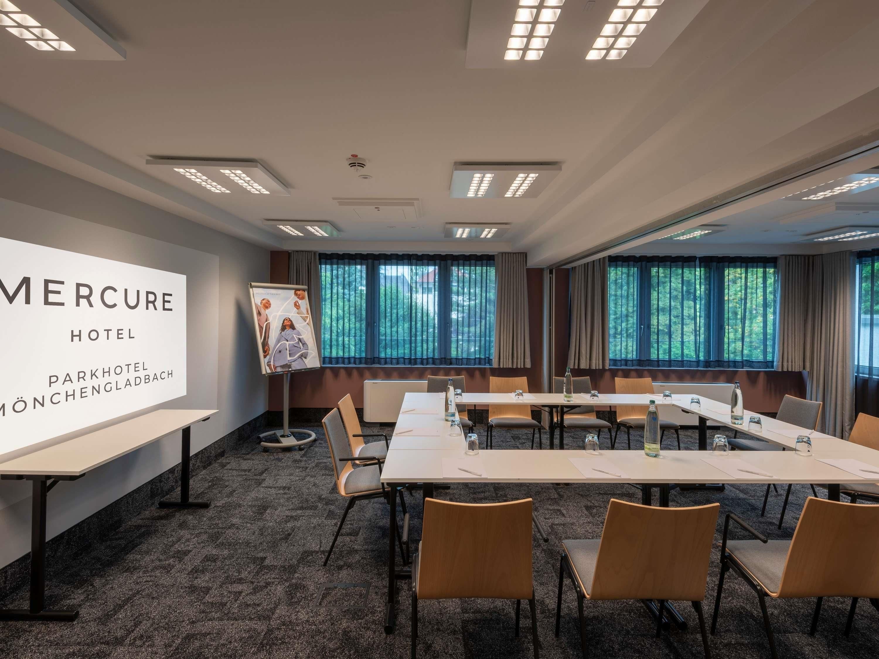 A conference room with a long table, chairs, and a large screen displaying the hotel name.