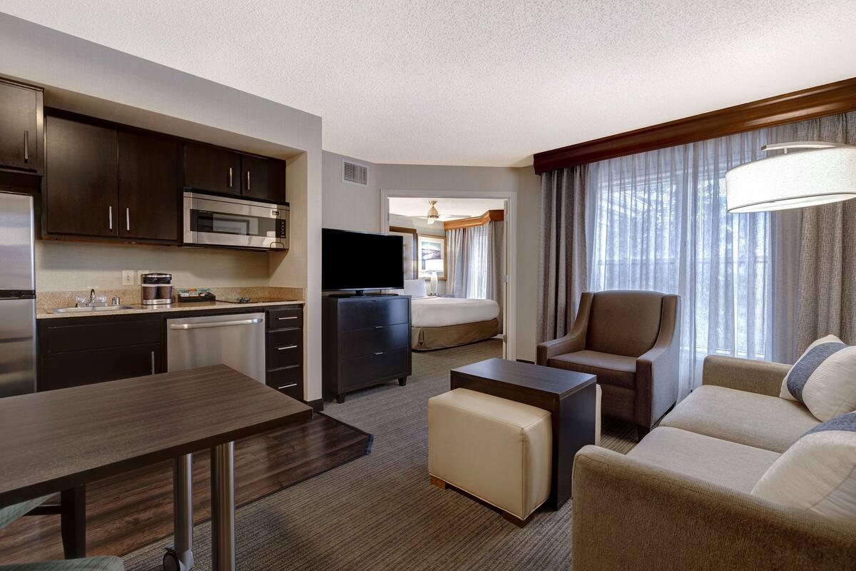 A hotel room with a kitchenette, a bed, a TV, a sofa, and a dining area.