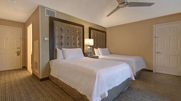 A hotel room with two beds, a ceiling fan, a lamp, and a carpeted floor.