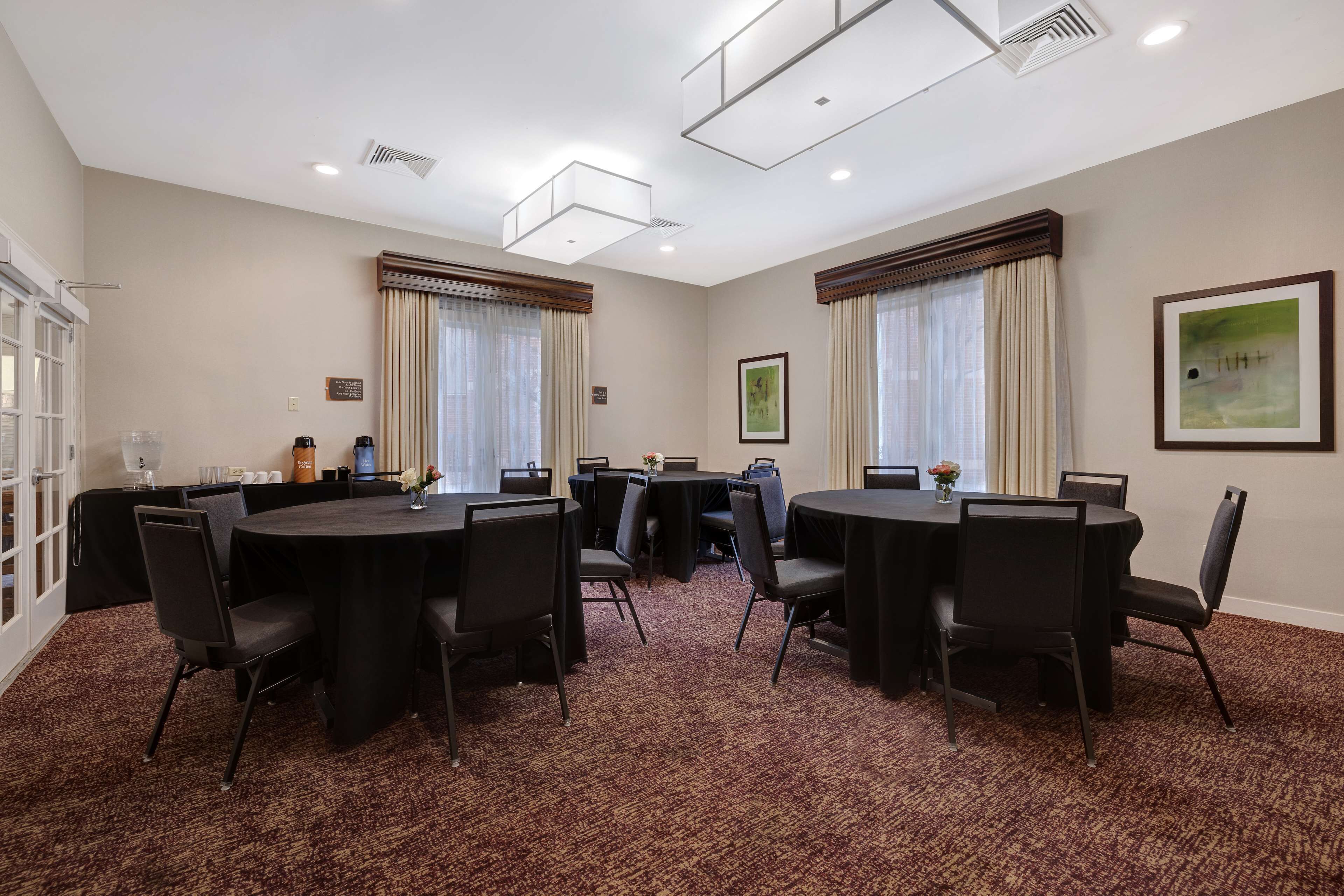 A conference room with round tables and chairs, a carpeted floor, and ceiling lights.