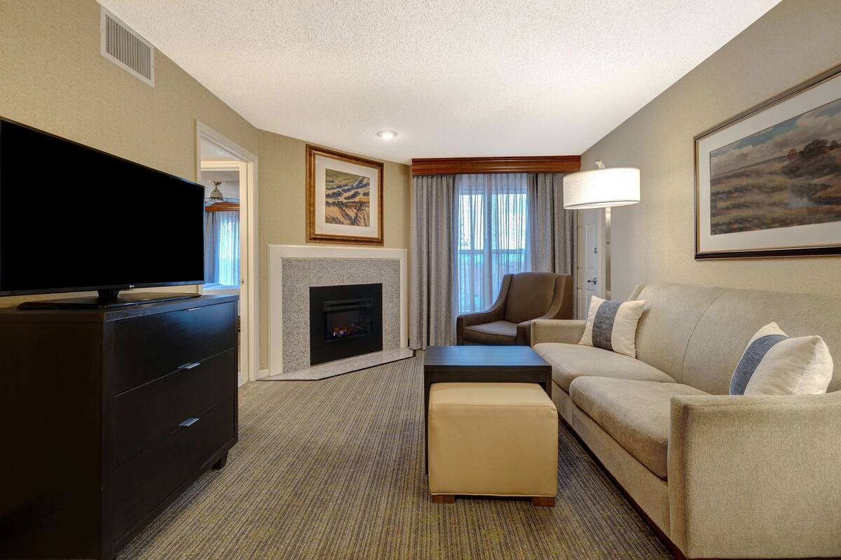 A hotel room with a flat-screen TV, a fireplace, a sofa, a coffee table, and a lamp.