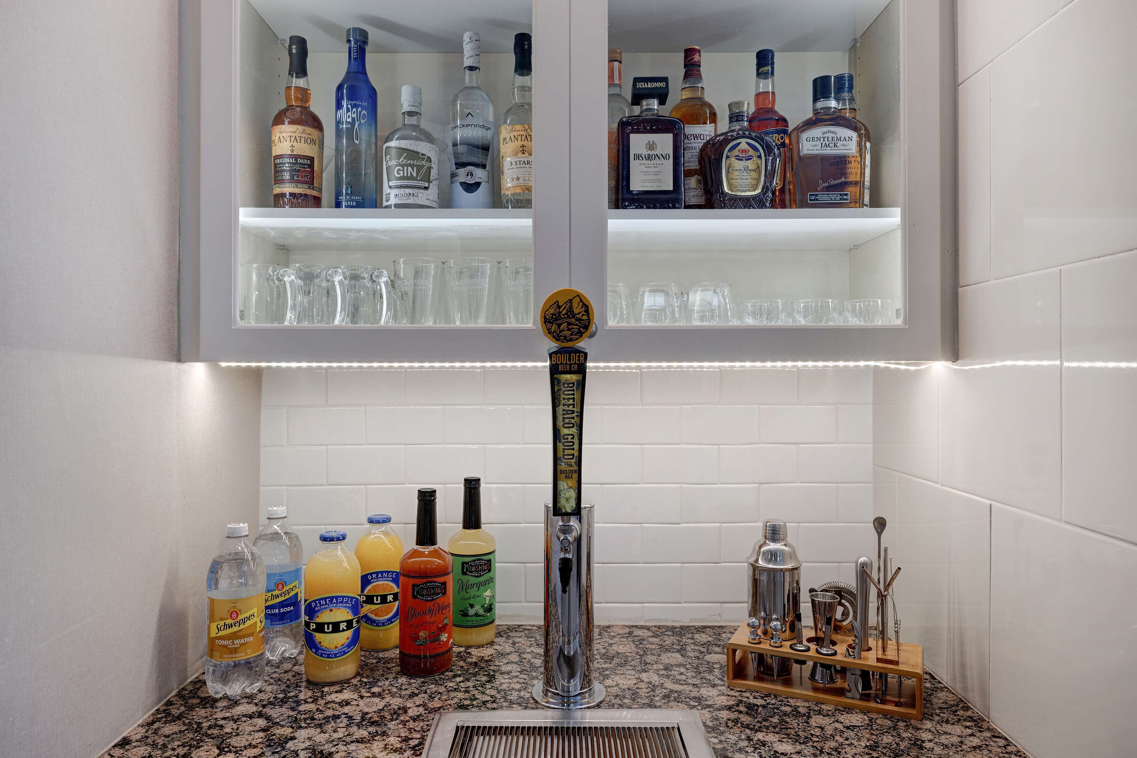 A bar area with a tap, shelves with liquor bottles, and various bottles and glasses on the counter.