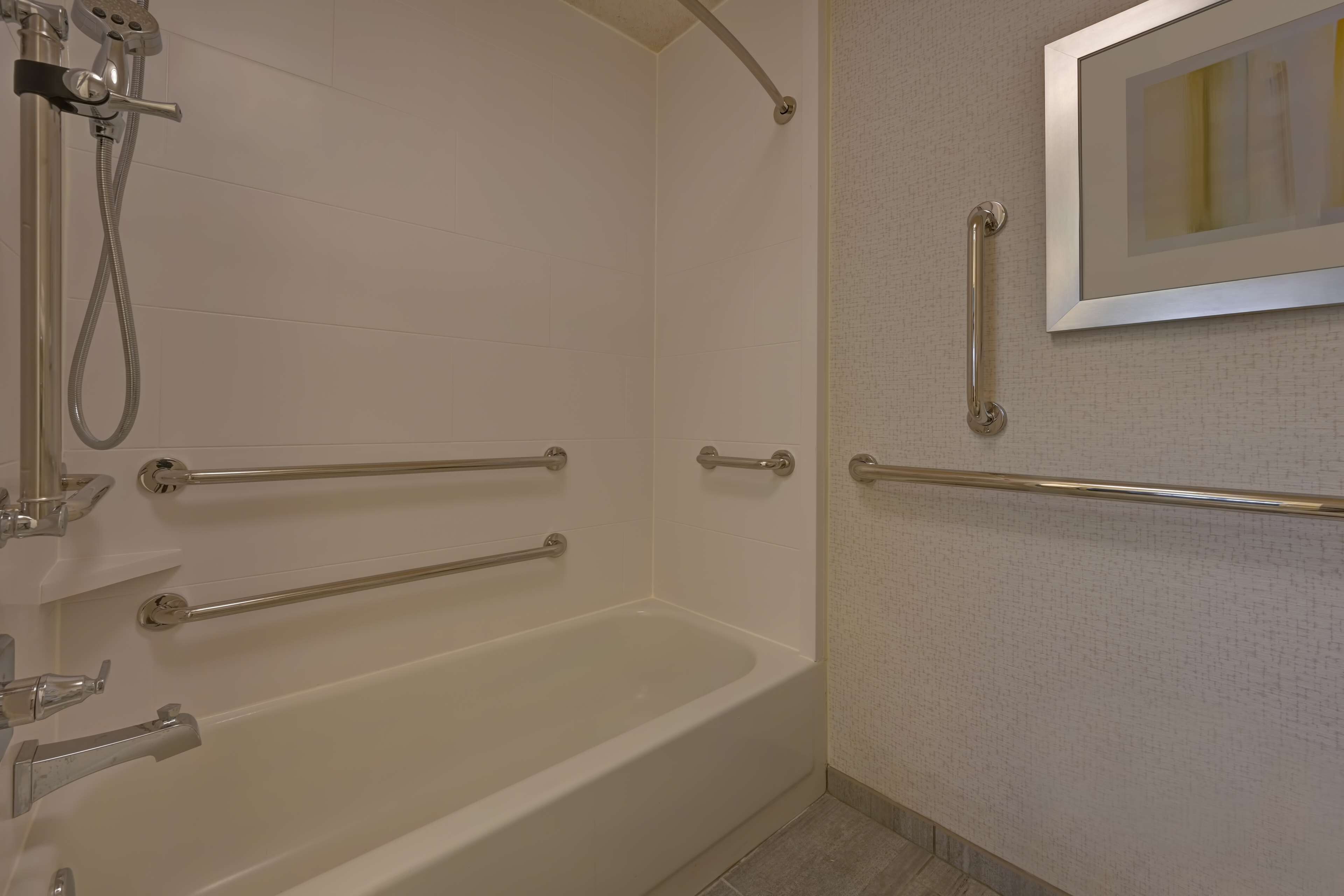 Un baño con bañera, barras de apoyo y ducha.