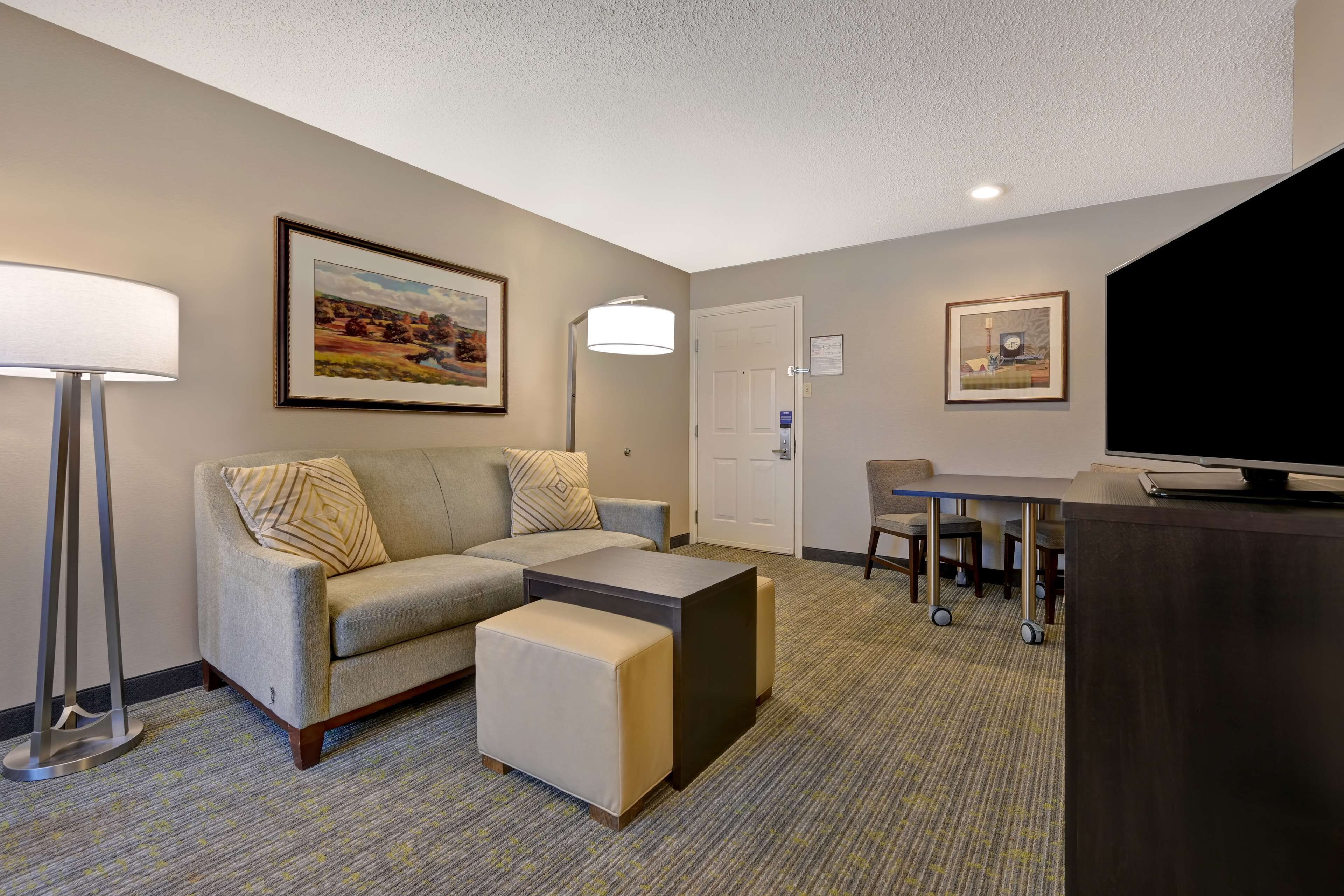 A hotel room with a sofa, ottoman, a flat-screen TV, a desk, and a chair.