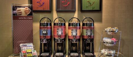 Una estación de café con cuatro cafeteras, una exhibición de sobres de café y una bandeja con pastelería.