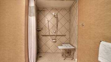 A small, tiled shower area with a showerhead, grab bar, and a small table.