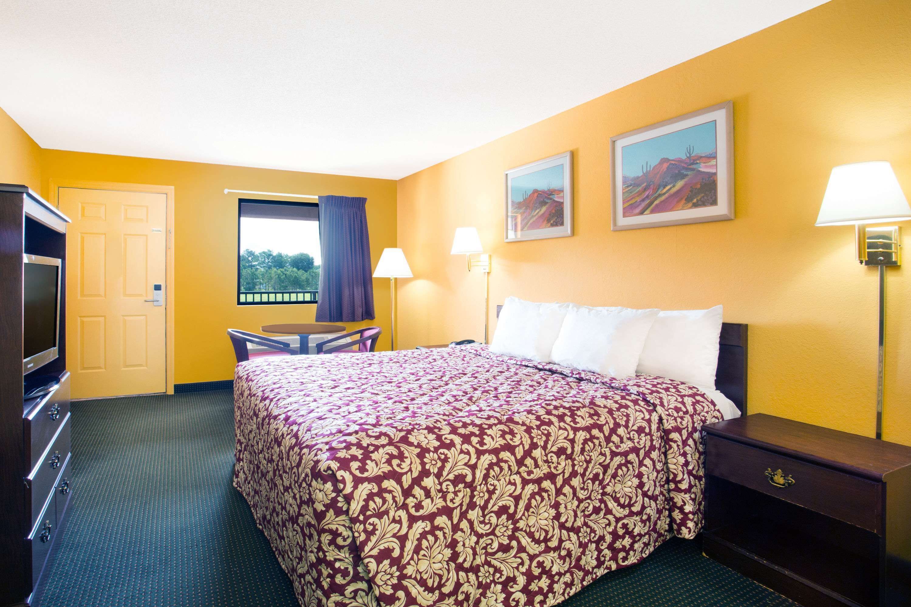 A hotel room with a large bed, a desk, a TV, and a window with curtains.