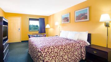 A hotel room with a large bed, a desk, a TV, and a window with curtains.