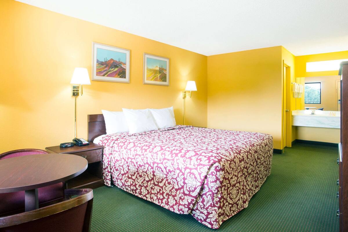 A hotel room with a bed, two bedside lamps, a desk, and a chair. There are two paintings on the wall above the bed.