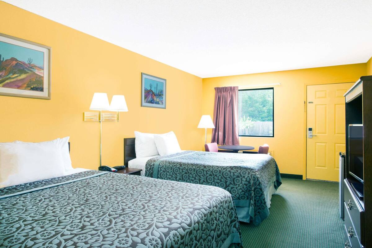 A hotel room with two beds, a desk, a chair, a TV, and a window with curtains.