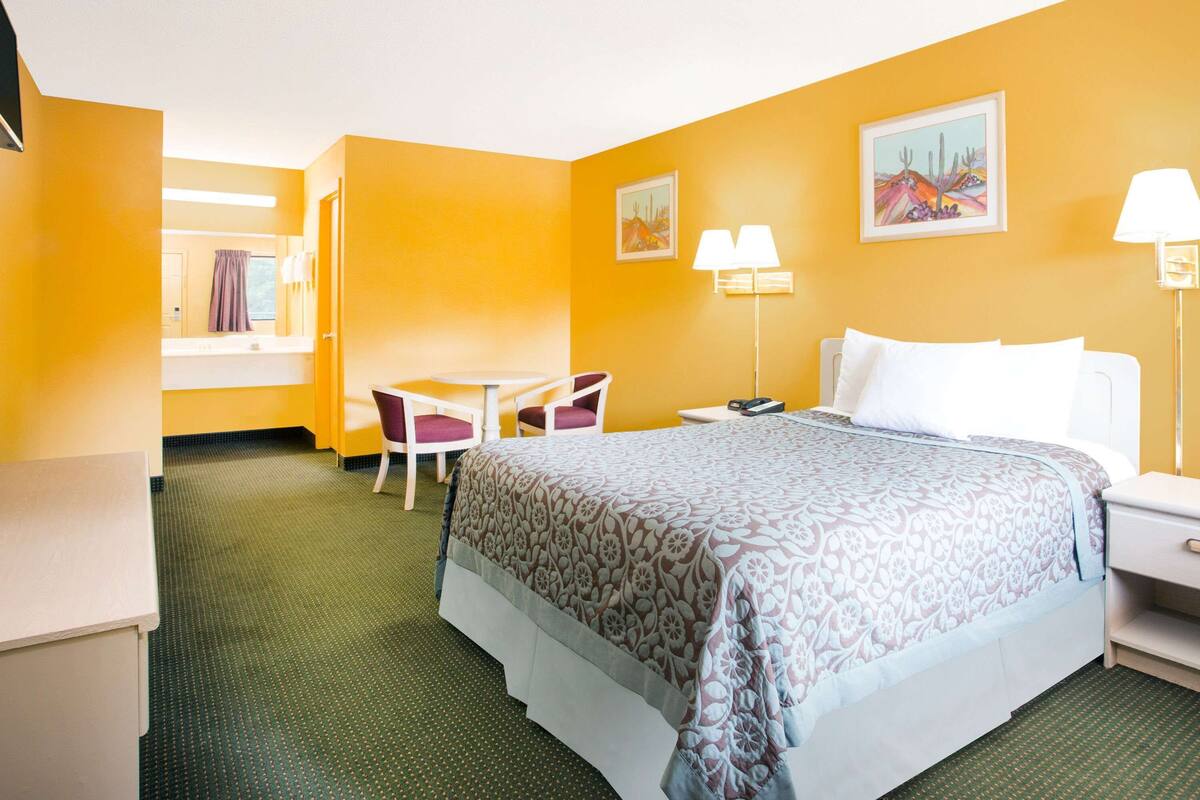 A hotel room with a bed, a desk, a chair, and two paintings on the wall.