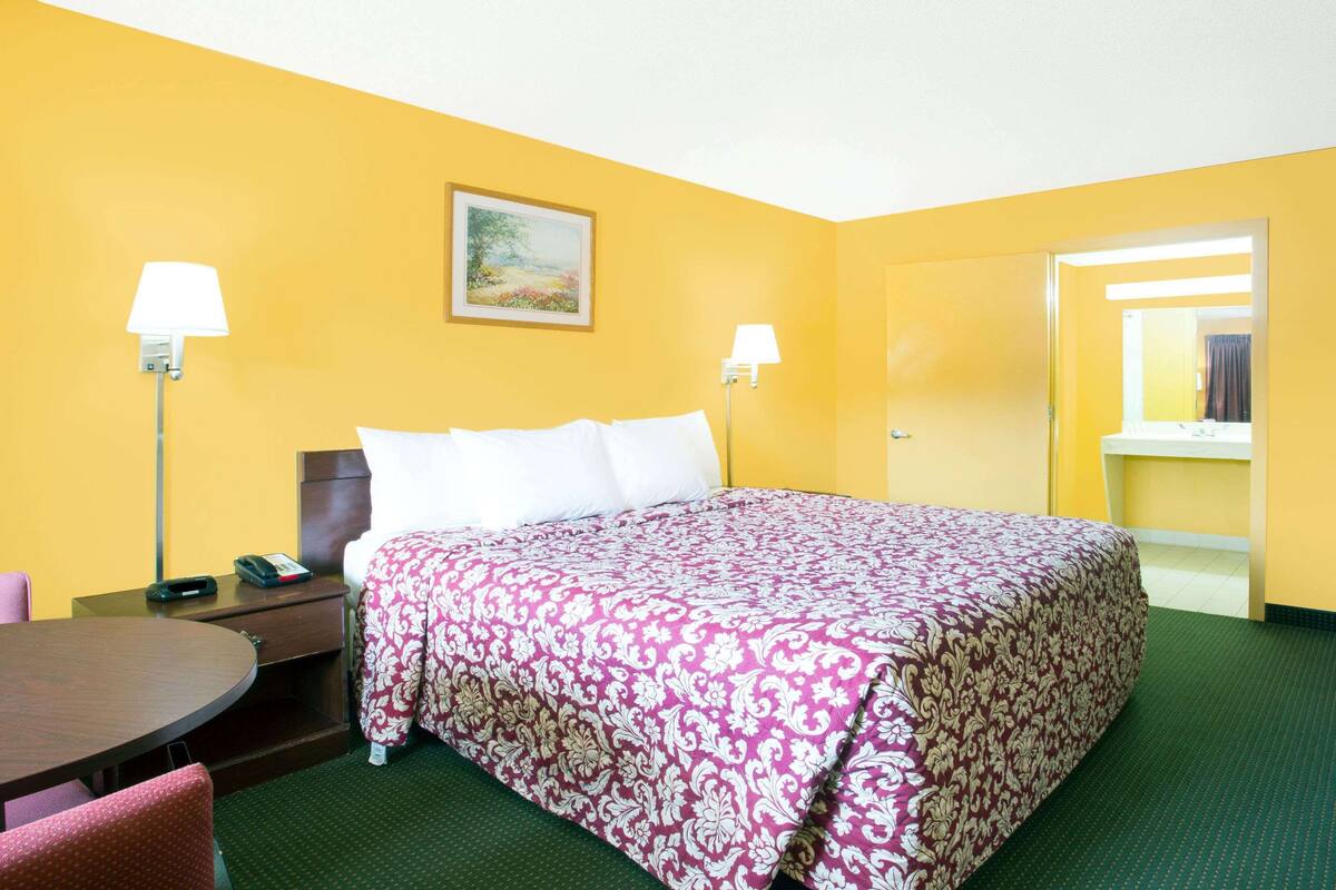 A hotel room with a bed, two bedside lamps, a desk with a telephone, and a painting on the wall.
