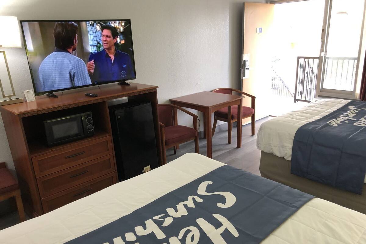 Ett hotellrum med en säng, en tv, ett skrivbord, en stol, en mikrovågsugn och ett litet kylskåp.