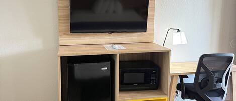 A compact room with a bed, a desk with a flat-screen TV, a microwave, and a chair.