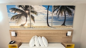 A hotel room with a bed, a headboard with a beach mural, two bedside tables, and a nightstand. - Days Inn by Wyndham Shorter (Shorter)