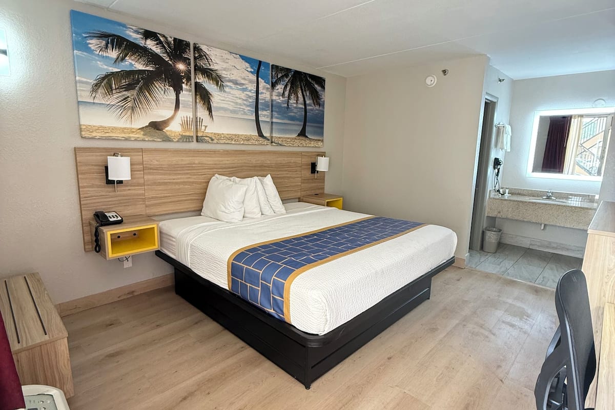 Ett hotellrum med en säng, ett skrivbord, en stol, en tavla som föreställer en strand och ett fönster.