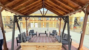 A covered outdoor seating area with a wooden swing set and a brick floor. - Days Inn by Wyndham Shorter (Shorter)