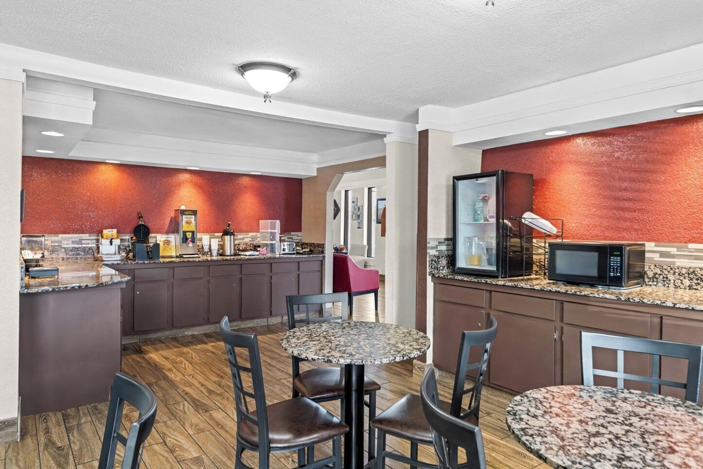 A modern kitchen with granite countertops, a microwave, and a refrigerator. There are two dining tables with chairs.