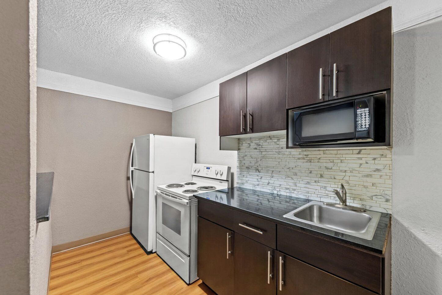 A compact kitchen with a refrigerator, stove, microwave, and sink.