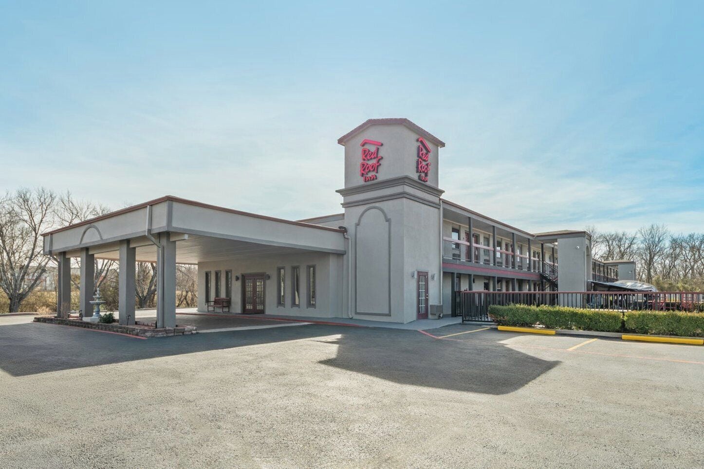 A hotel with a covered outdoor area, a central tower with signage, and a parking lot.