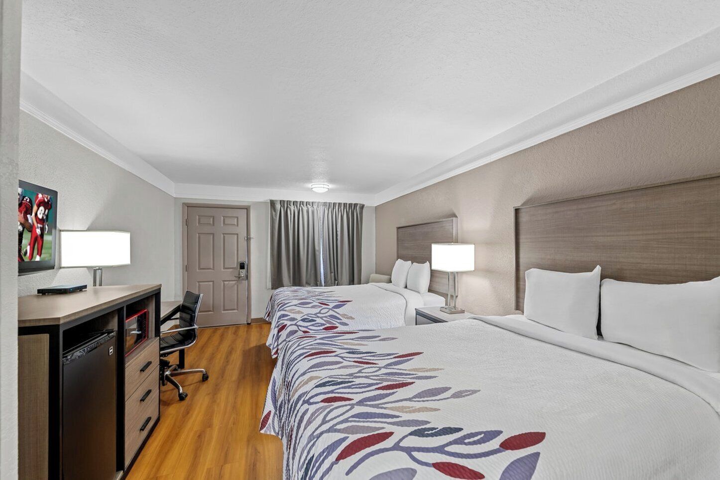 Una habitación de hotel con dos camas, un escritorio con silla, un televisor y una puerta.