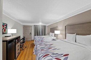 Una habitación de hotel con dos camas, un escritorio con silla, un televisor y una puerta.