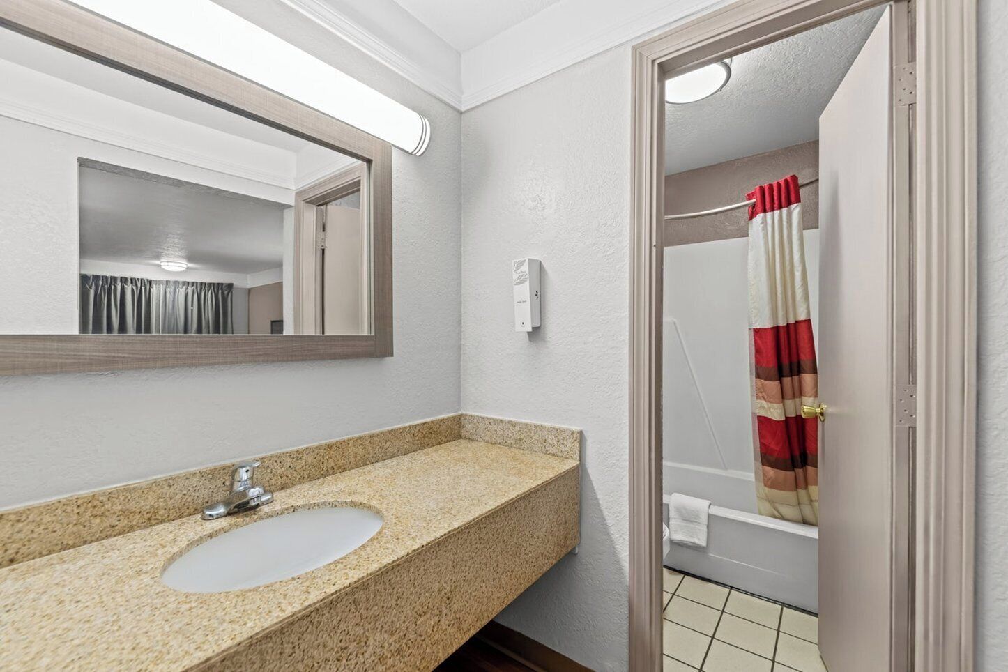 A bathroom with a granite countertop sink, a mirror, a shower curtain, and a towel rack.