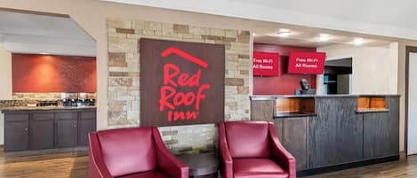 Zona de recepción de Red Roof Inn con pared de piedra, letrero, mostrador de recepción y dos sillones de cuero rojo.