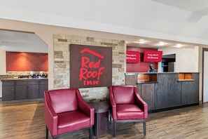 A Red Roof Inn reception area with a stone wall, a signboard, a reception desk, and two red leather chairs. - Red Roof Inn Ardmore (Ardmore)